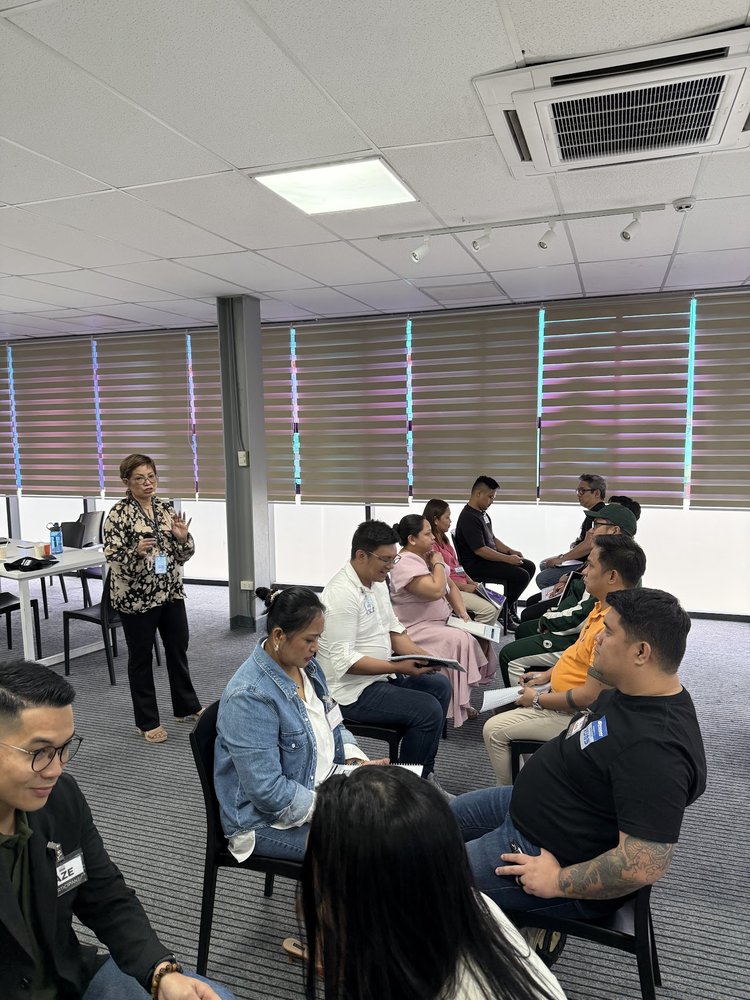 Coach Gina Katigbak teaches the room with a microphone during a live coaching workshop.