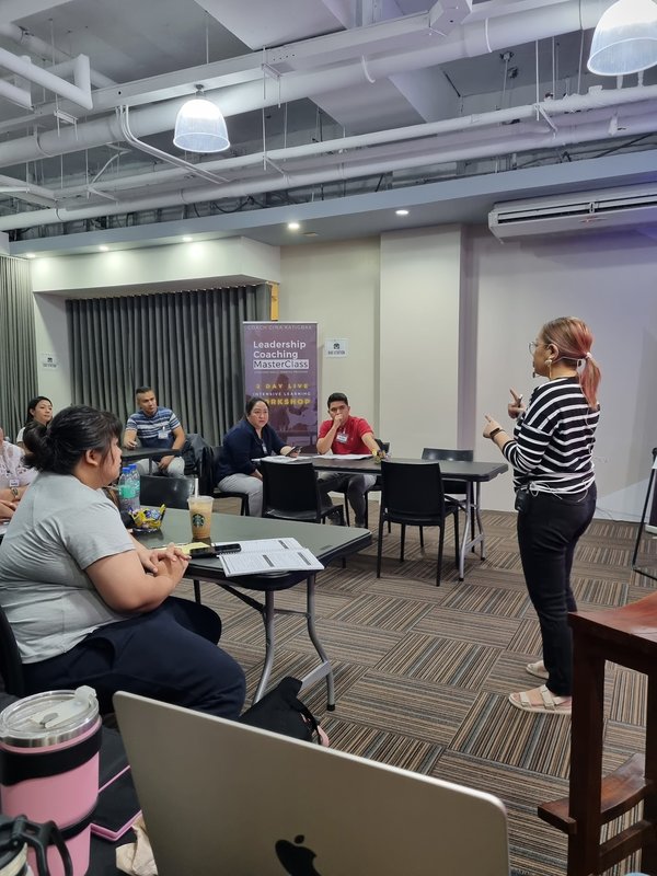 Coach Gina Katigbak smiles warmly at the front of the room beside her Leadership Coaching MasterClass banners.